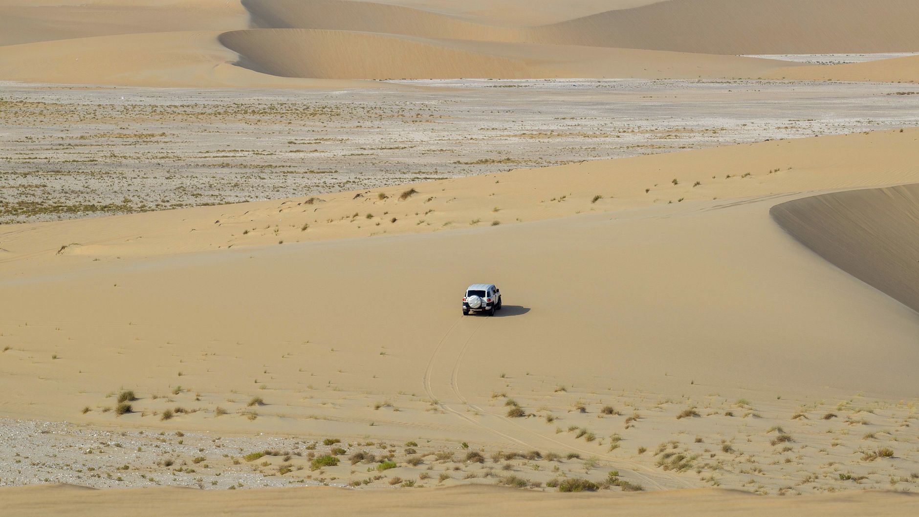 Picturesque drone view of SUV car driving along sandy dunes on sunny day in endless desert
