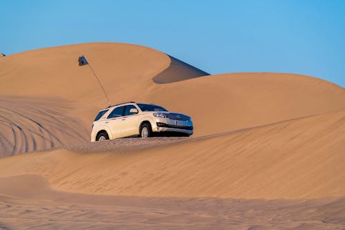 Modern off road car driving along desert sandy dunes against blue sky