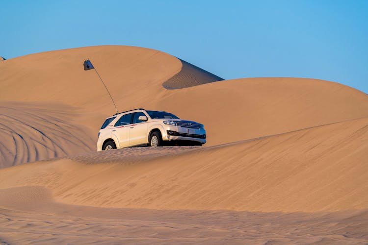 Modern Off Road Car Driving Along Desert Sandy Dunes Against Blue Sky