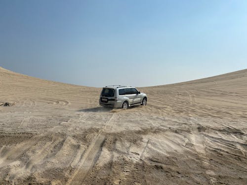 Modern off road car driving along rough sandy terrain during expedition trip in desert against cloudless blue sky