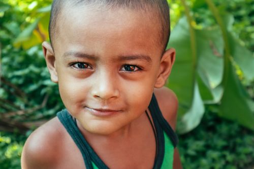 Free A cheerful young child looking at the camera with greenery in the background. Stock Photo