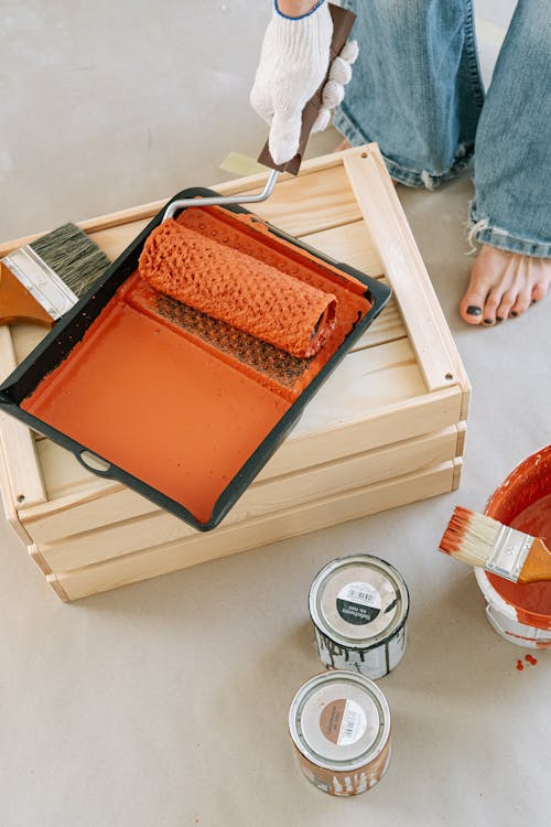 Close-Up Shot of a Person Holding a Paint Roller with Orange Paint