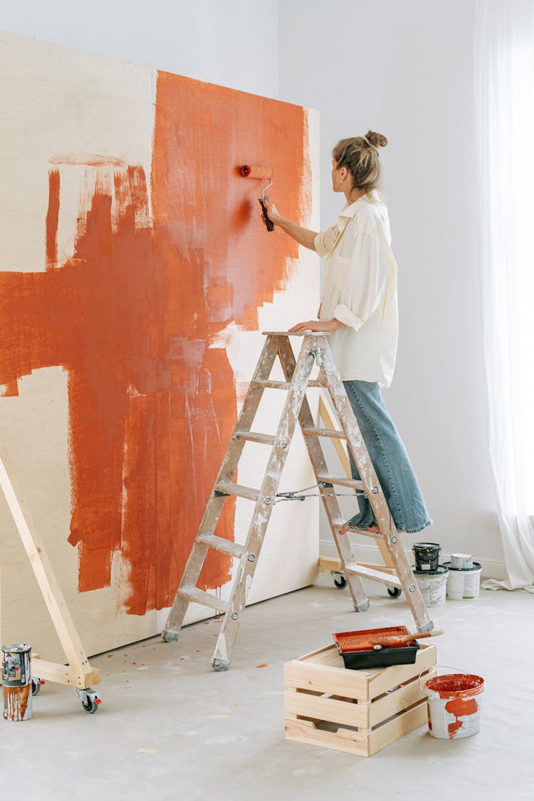 Woman Standing On A Stepladder Painting A Wall With A Roller