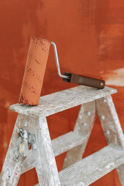 A paint roller rests on a stepladder against a painted wall, capturing a home renovation scene.
