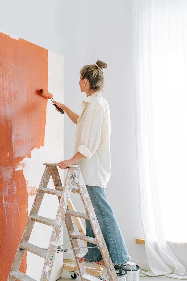 A Woman On A Ladder Painting A Wall 