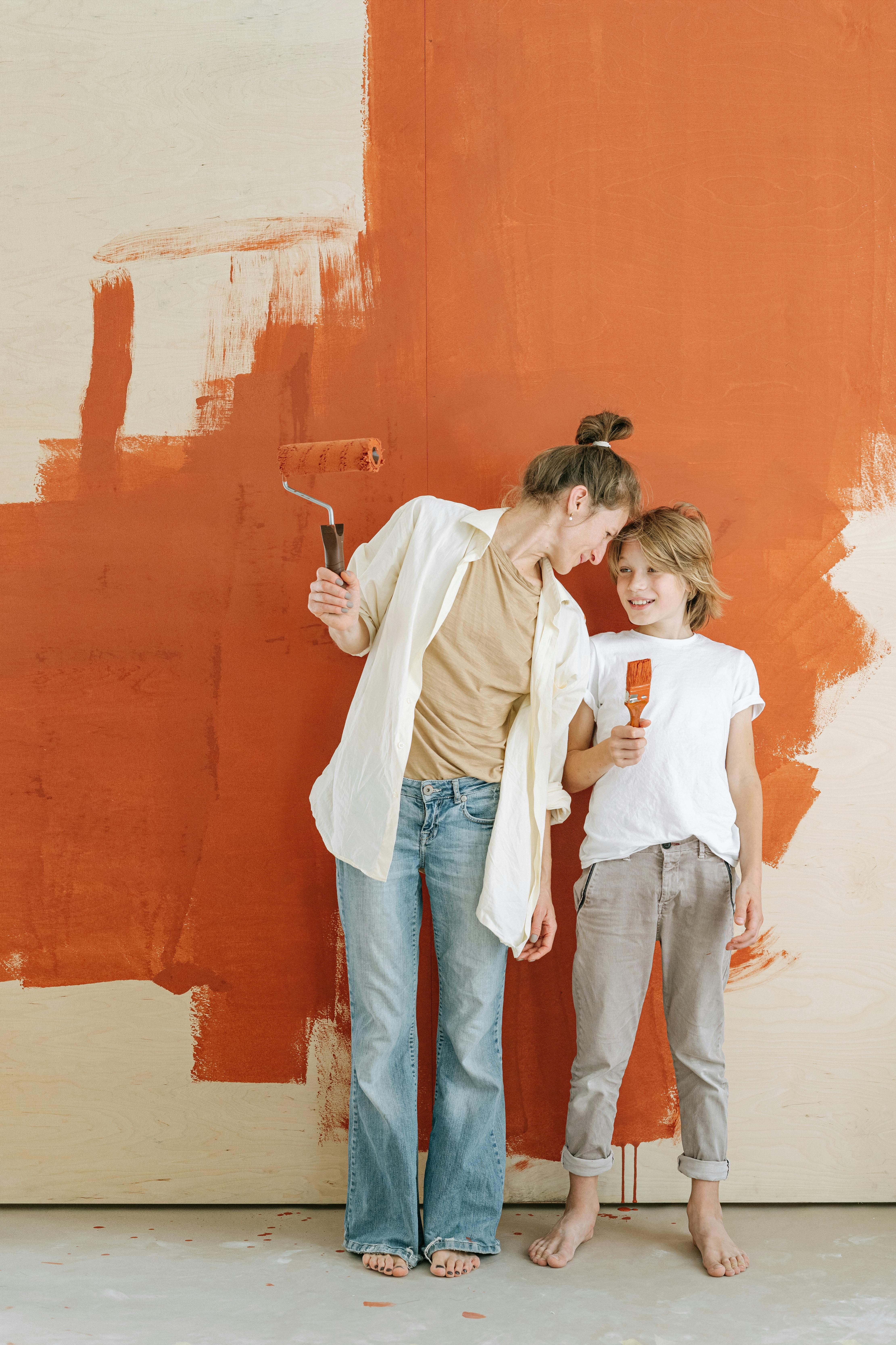 woman with a paint roller standing beside a boy holding paintbrush