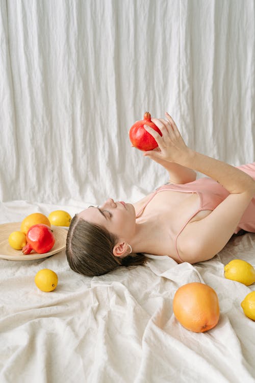 Free A Woman Holding a Pomegranate While Lying Down  Stock Photo