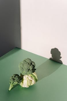 Broccoli and cauliflower with shadows on a green surface, captured in natural light.