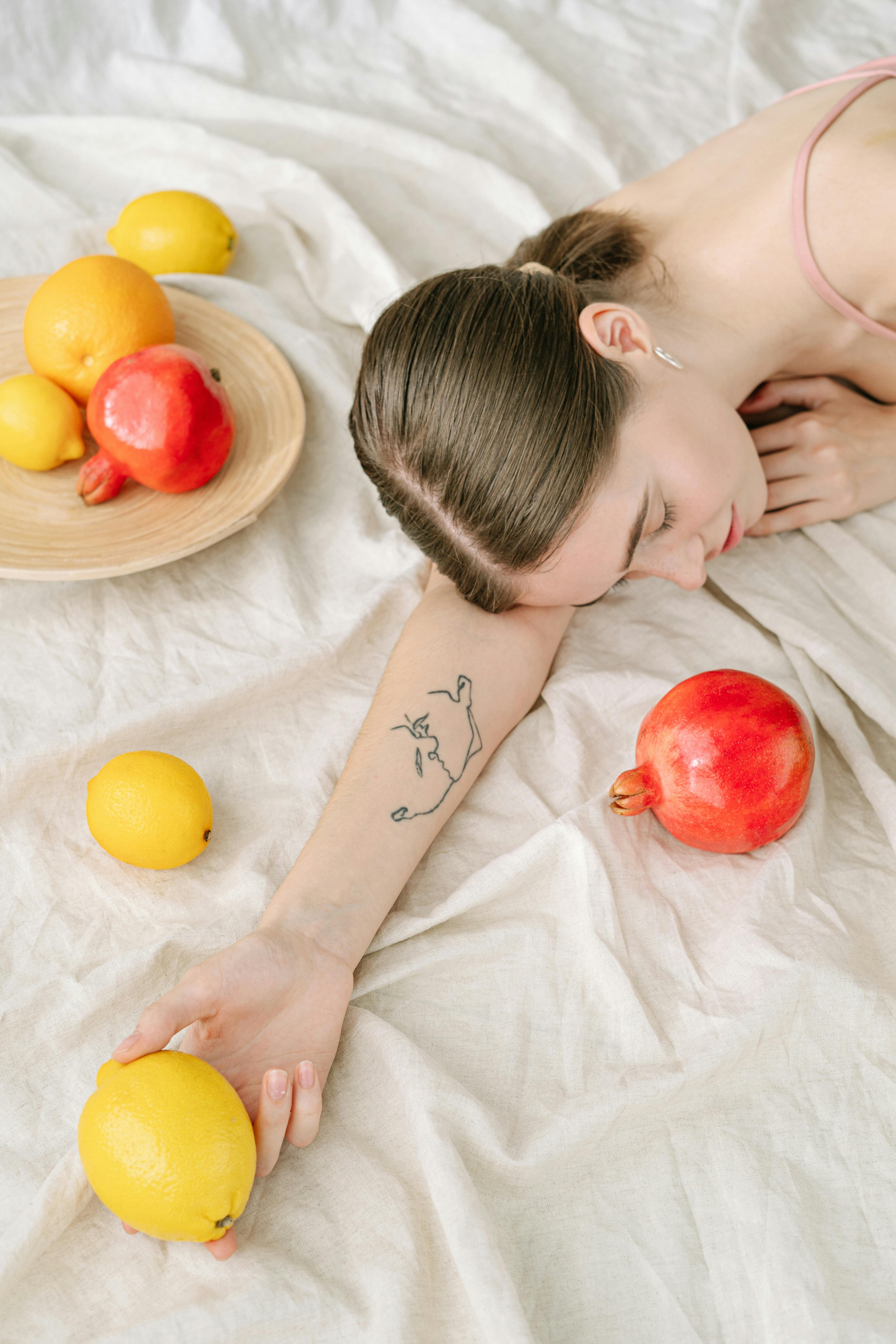 一名妇女躺在亚麻布上，周围散落着柠檬和石榴，展示着她的纹身