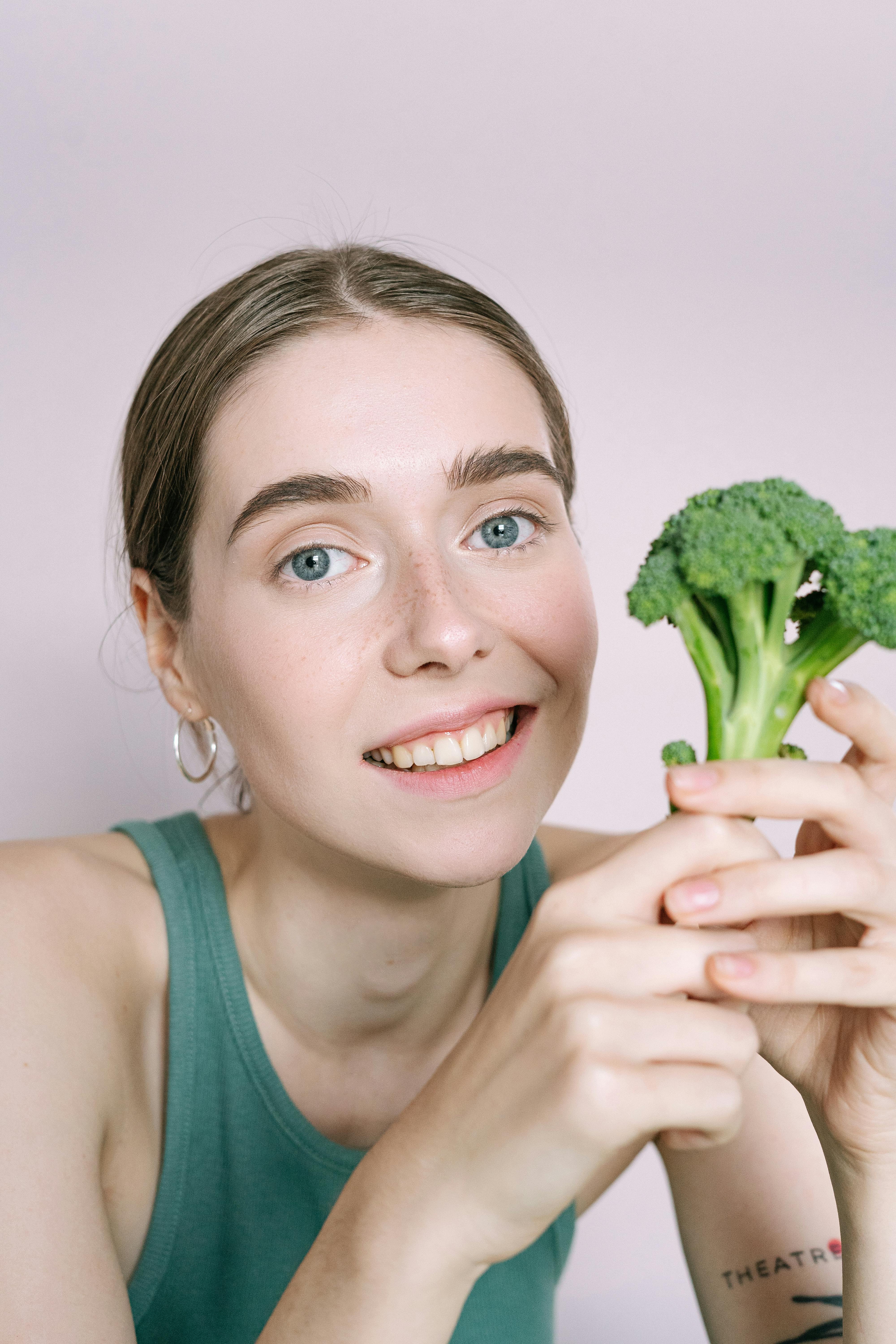 Cheerful woman holding a fresh broccoli head and smiling at the camera.