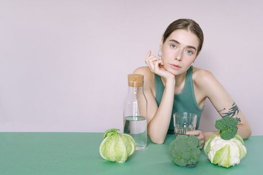 一名年轻女子身穿绿色上衣坐在那里，手里拿着蔬菜和一杯水