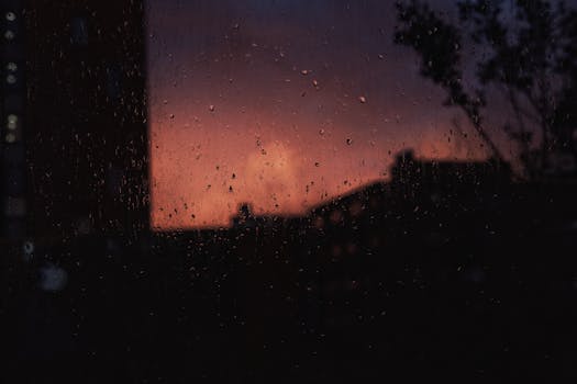 View of a stunning sunset silhouette through a rainy window, creating a moody and reflective ambiance.