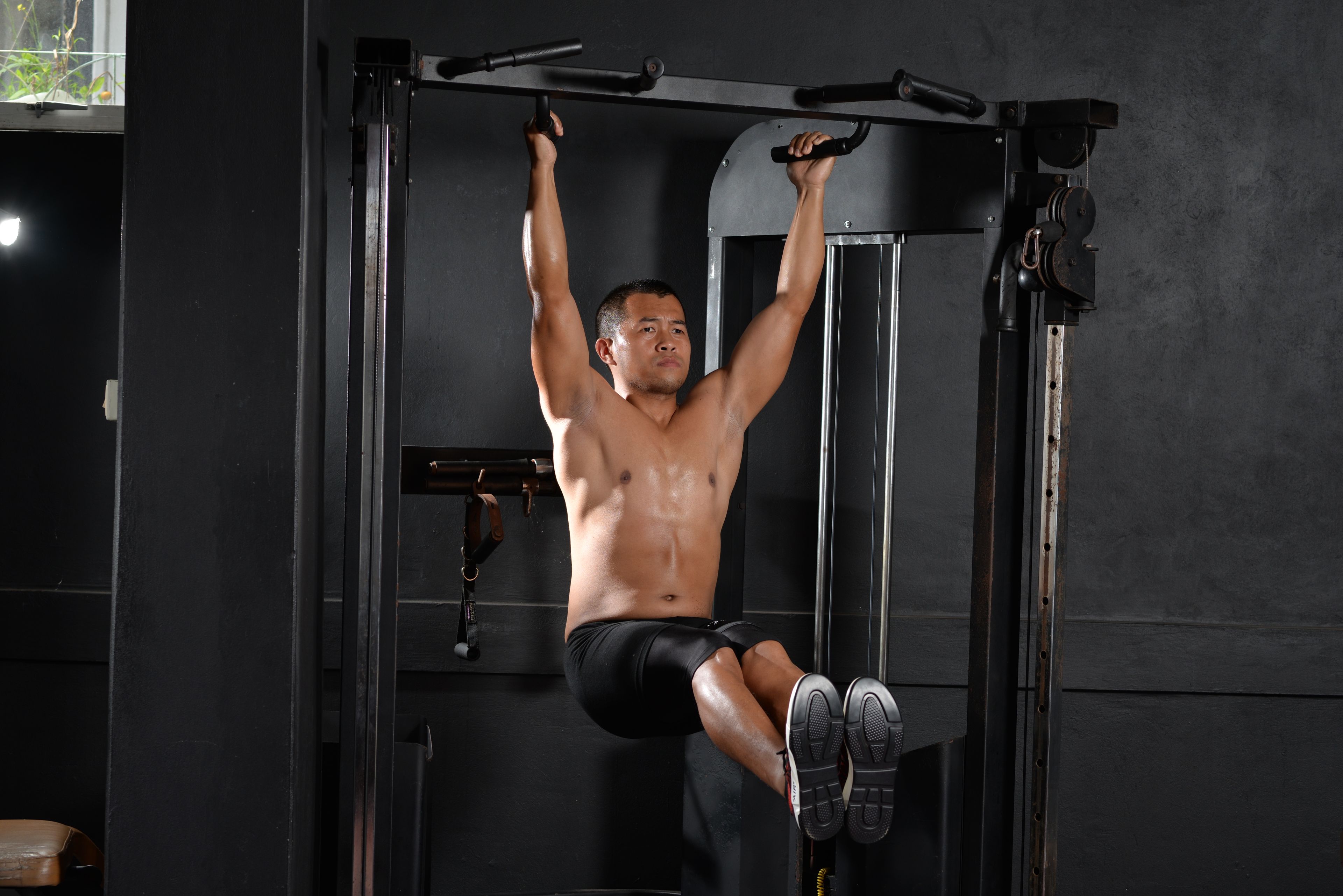 A shirtless man doing a workout with pull-up bar indoors at a gym, showcasing fitness and strength.