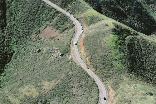 Asphalt highway with cars along peak of green hills
