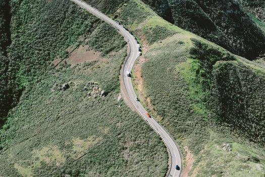 Drone view of curvy road going through countryside between green highlands on summer sunny day
