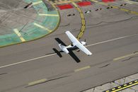 From above of small biplane landing on runway with cracks and yellow markings on summer sunny day