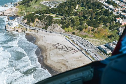 Free Protest on seashore with large group of people seen from plane gathered in shape of resist word on sunny day Stock Photo