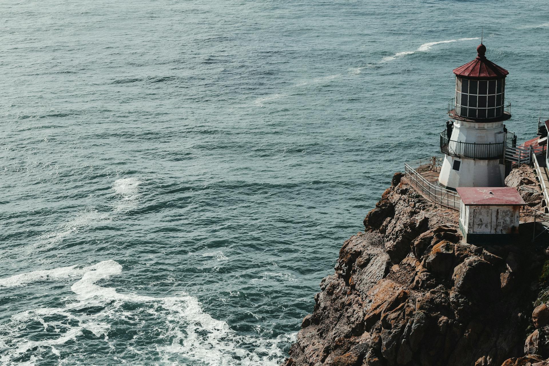 From above of small shabby beacon on top of rocky cliff with waving ocean below