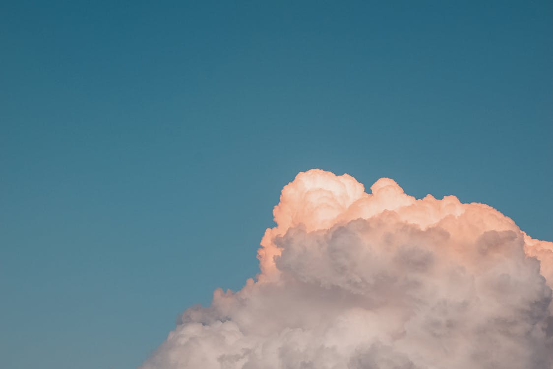 Minimalist landscape of fluffy cloud colored in sunset light floating in blue sky