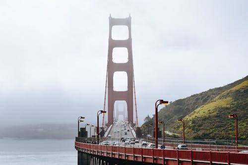 Golden Gate Bridge with cars driving on roadway along green hills in dense fog