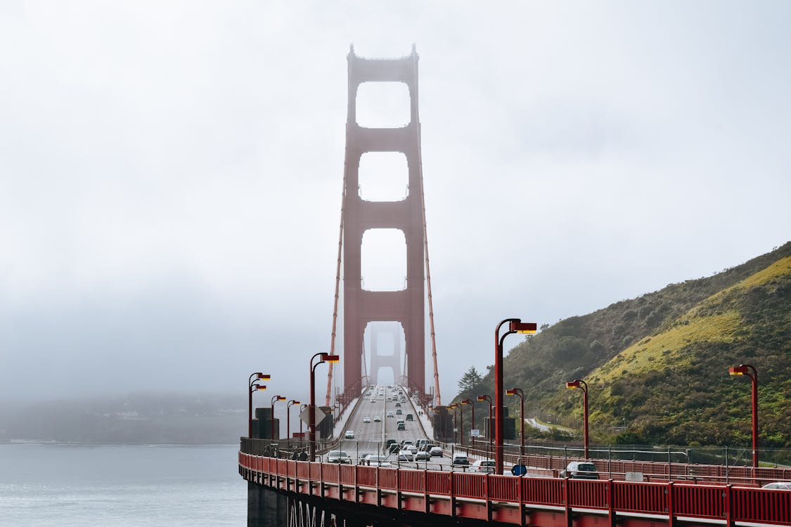 Golden Gate Bridge with cars driving on roadway along green hills in dense fog
