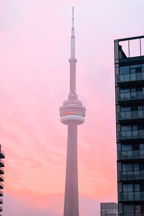 Hazy construction of CN tower among skyscrapers against colorful sunset sky in Toronto