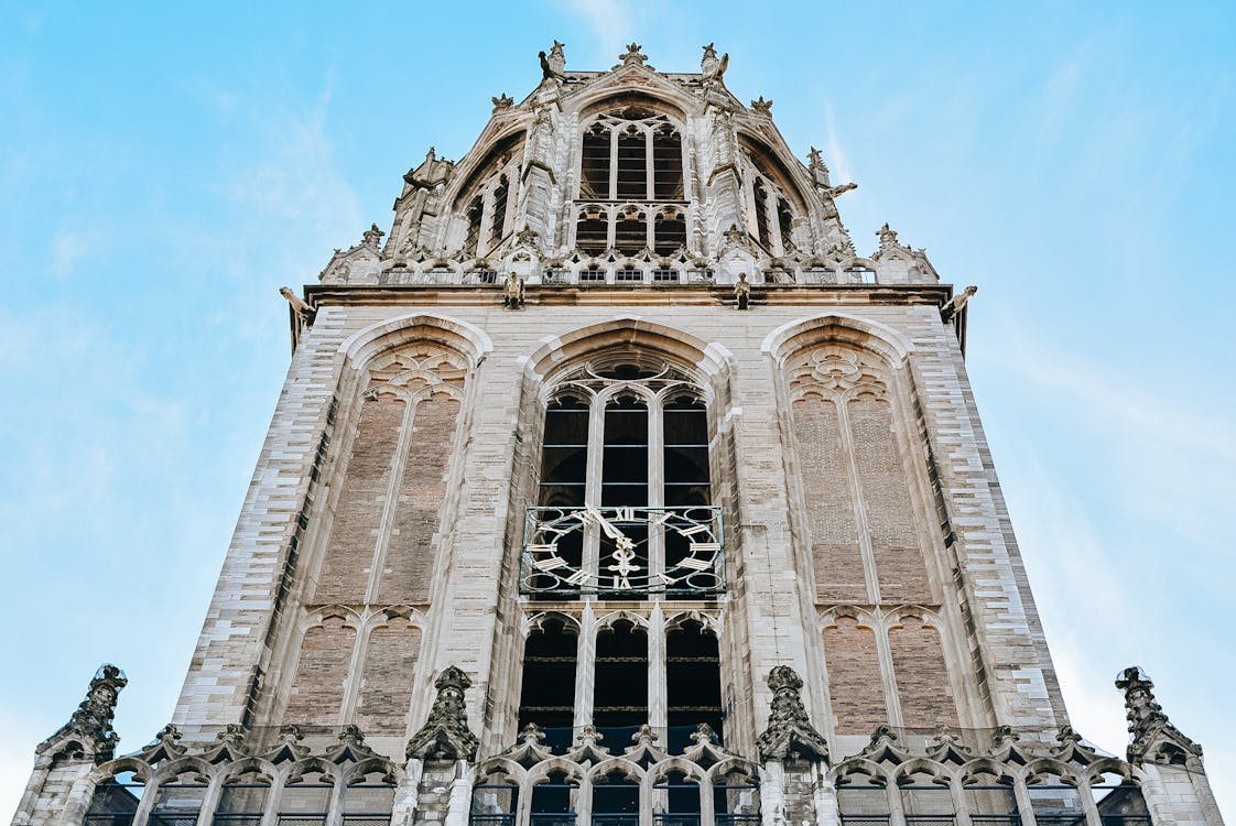 From below Gothic exterior of Dom Tower with clock and ornaments in city of Utrecht