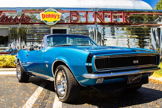 Vintage blue Chevrolet Camaro parked in front of Denny's Classic Diner under sunny skies.