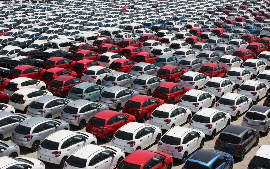 Overhead shot of neatly parked colorful cars in a large outdoor lot under sunlight