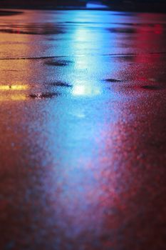 Vivid light reflections on a wet pavement create a colorful display at night.