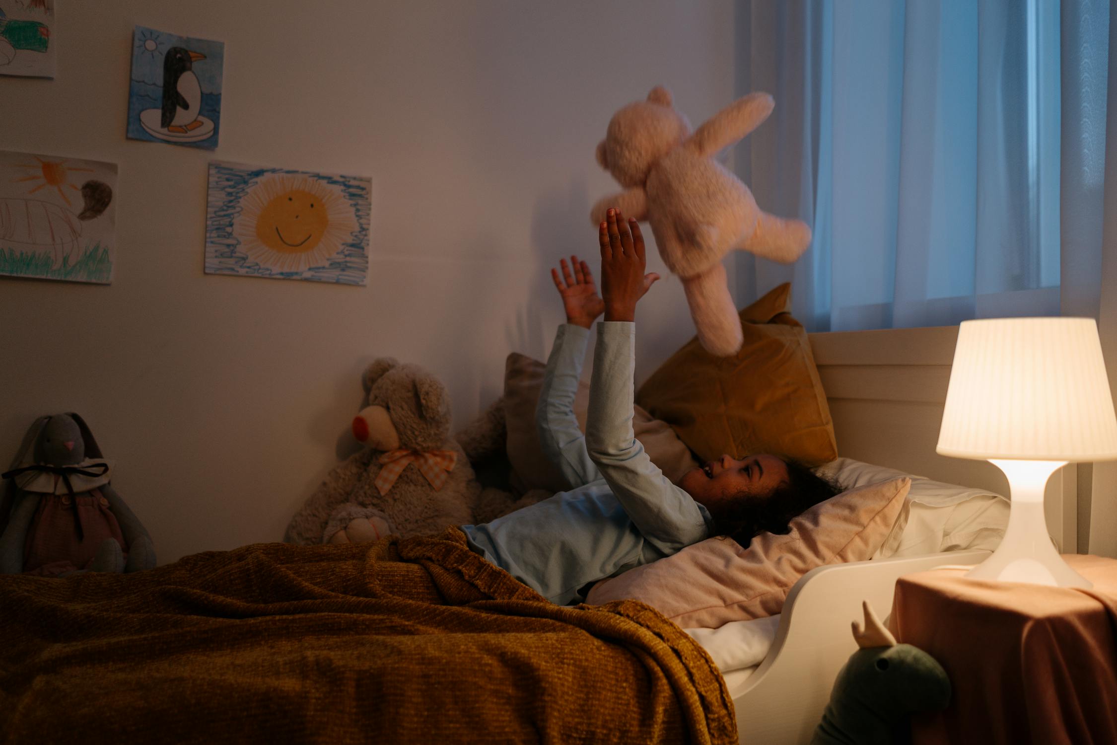 Image of girl laying in bed throwing her teddy bear in the air