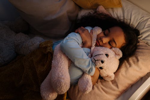 Free An Adorable Girl Hugging Her Teddy Bear while Sleeping Stock Photo