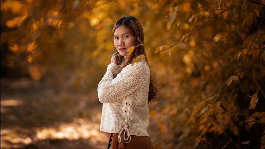Woman wearing a knitted sweater among golden autumn leaves
