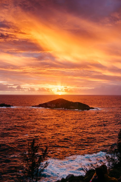 Magnificent scenery of rocky formations in rippling ocean with foamy waves crashing near coast against picturesque colorful sunset sky in Arraial do Cabo