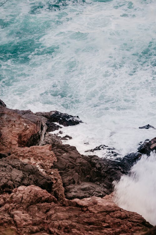 Powerful foamy sea waves washing rocky cliff