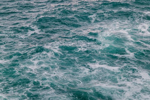 High angle of foamy waves of powerful turquoise ocean with uneven surface in sunlight