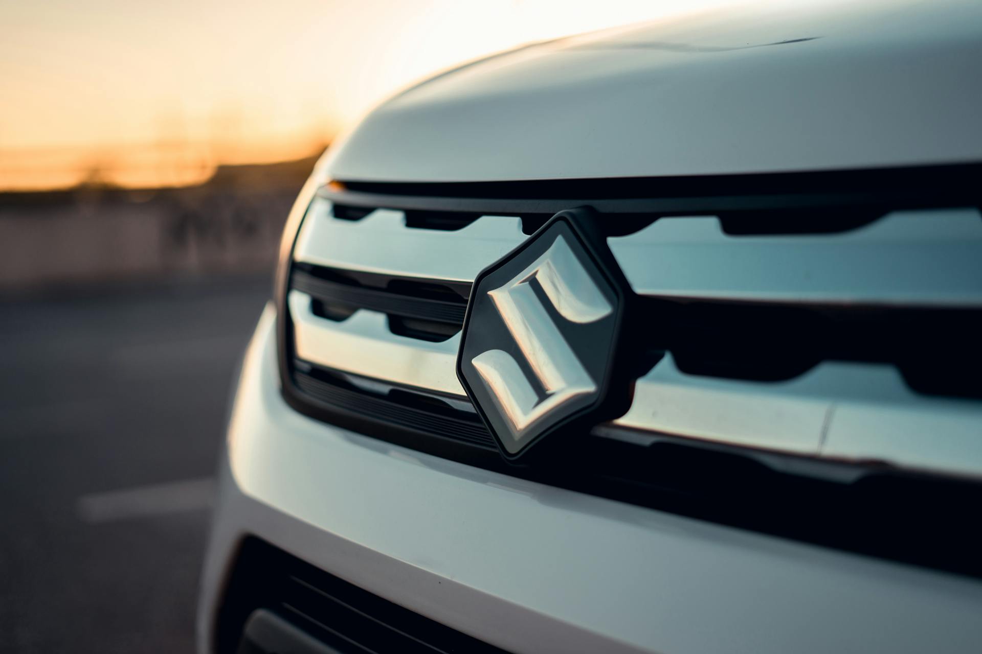 Detailed view of Suzuki car grille and logo captured at sunset, showcasing modern automotive design.