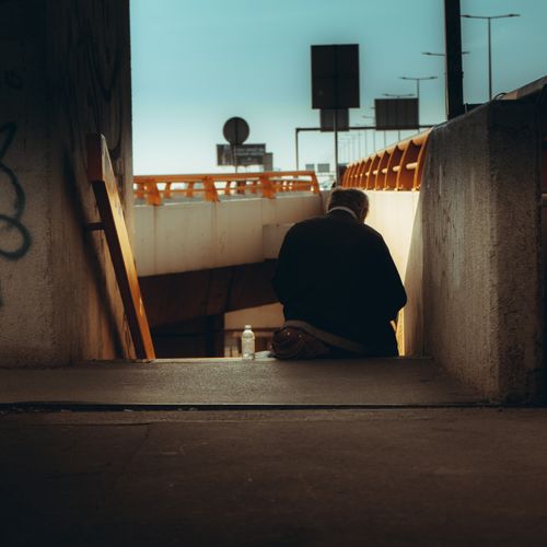 Free A solitary figure sits on concrete stairs in an urban setting during twilight, creating a contemplative mood. Stock Photo