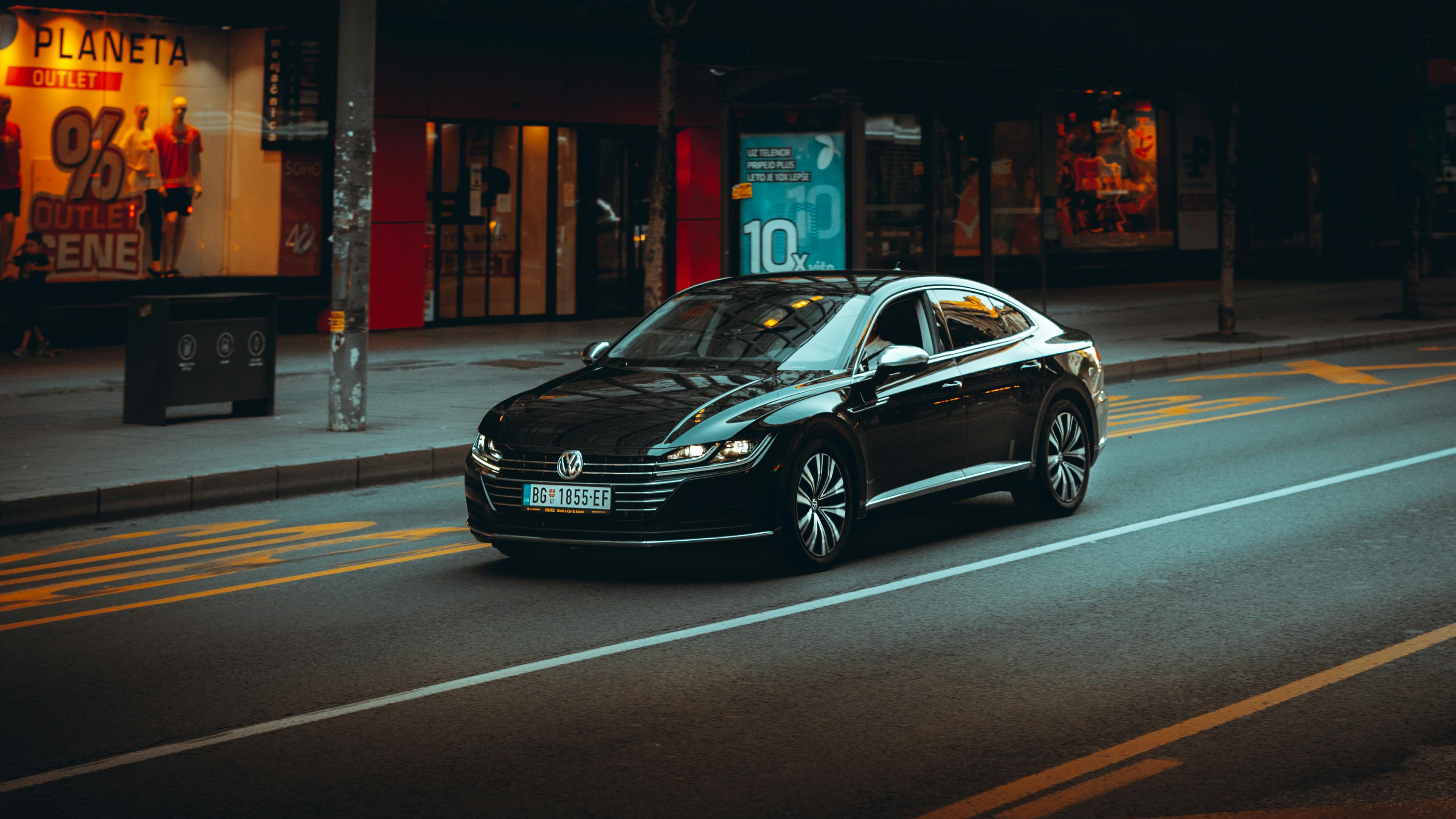 Free A sleek black sedan cruises down an urban road during nighttime. Stock Photo