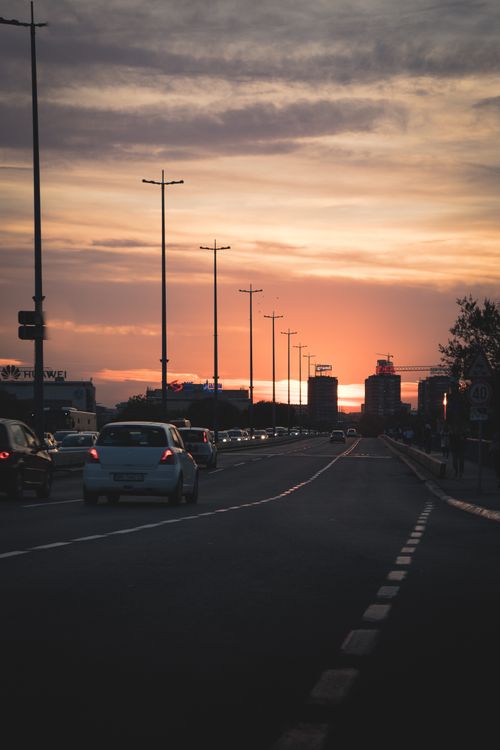 Free Cars drive on a city highway during a stunning sunset, capturing urban life's dynamic atmosphere. Stock Photo