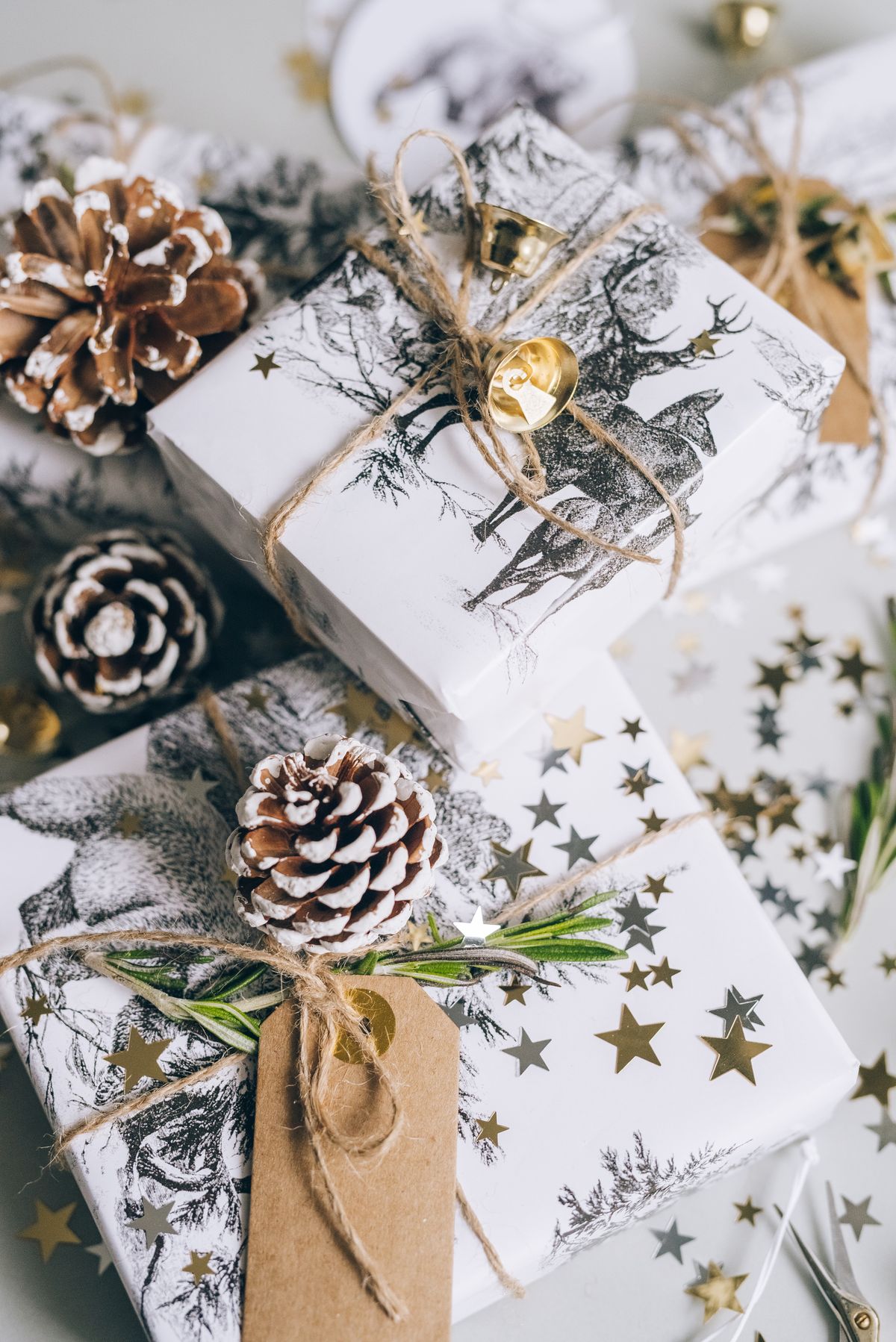 Small Christmas gifts wrapped in white paper with twine, pine cones, a kraft tag and star confetti