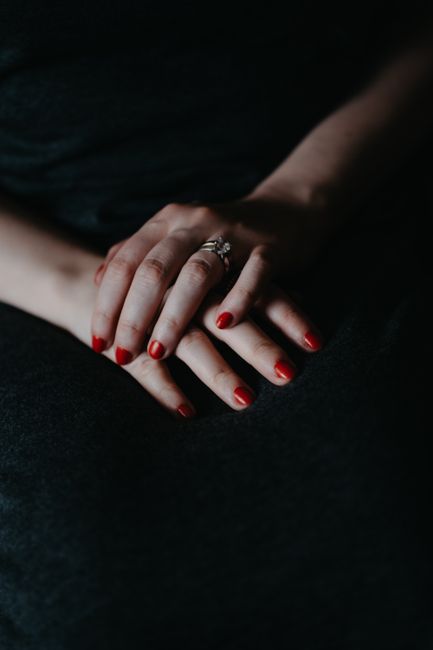 Close-up of a woman's hands with red nails and a ring, showcasing elegance.