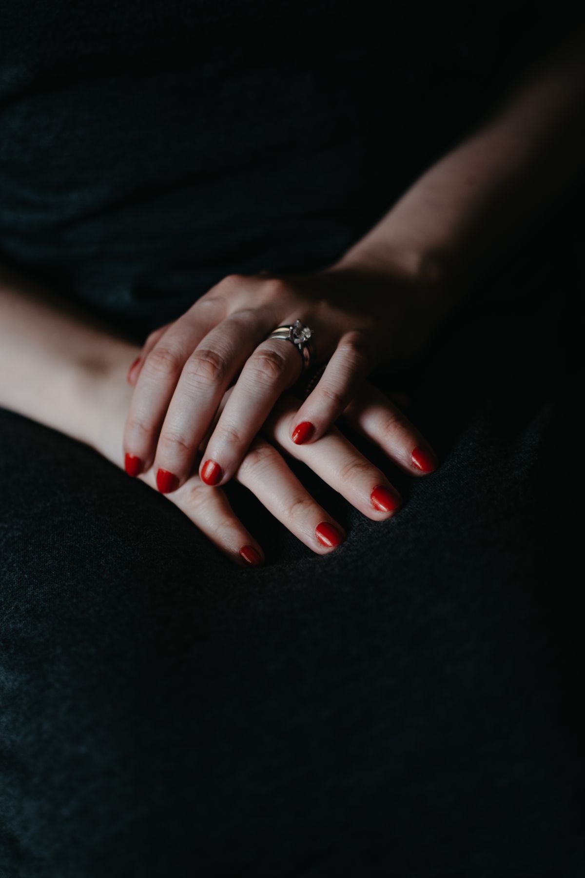 Close-up of a woman's hands with red nails and a ring, showcasing elegance.