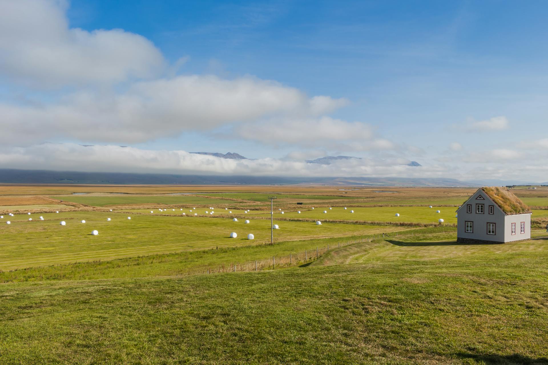 Beautiful Icelandic countryside with a quaint cottage and hay bales under a clear blue sky.