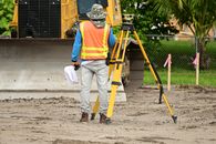 Person in Orange and Yellow Jacket and White Pants Holding Black and Yellow Camera