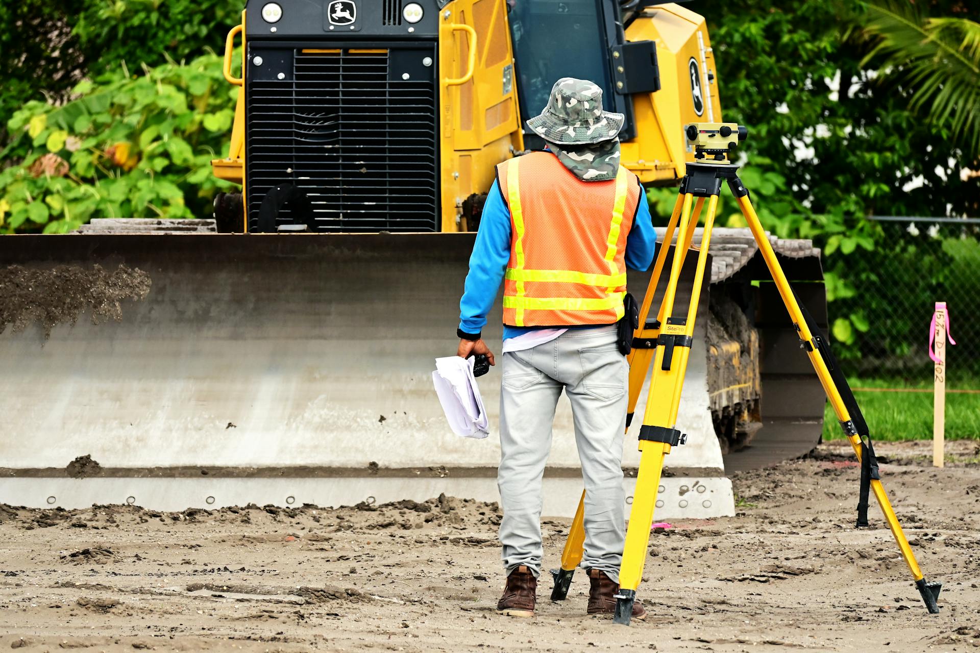 Surveyor with equipment at an active construction site, observing bulldozer operations.