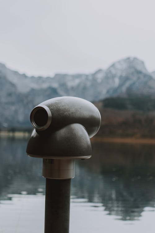 Tourist binocular on coast of calm pond near rocky mountains in autumn highland