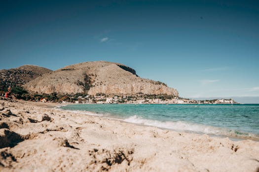 A stunning summer beach in Sicily with a rocky mountain and clear blue waters.