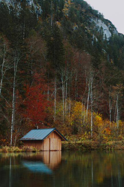 Calm pond with submerged abandoned structure under rocky mountain with vegetation in autumn