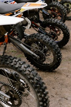 Close-up of dirt bikes parked on muddy ground, showcasing tires and chains.